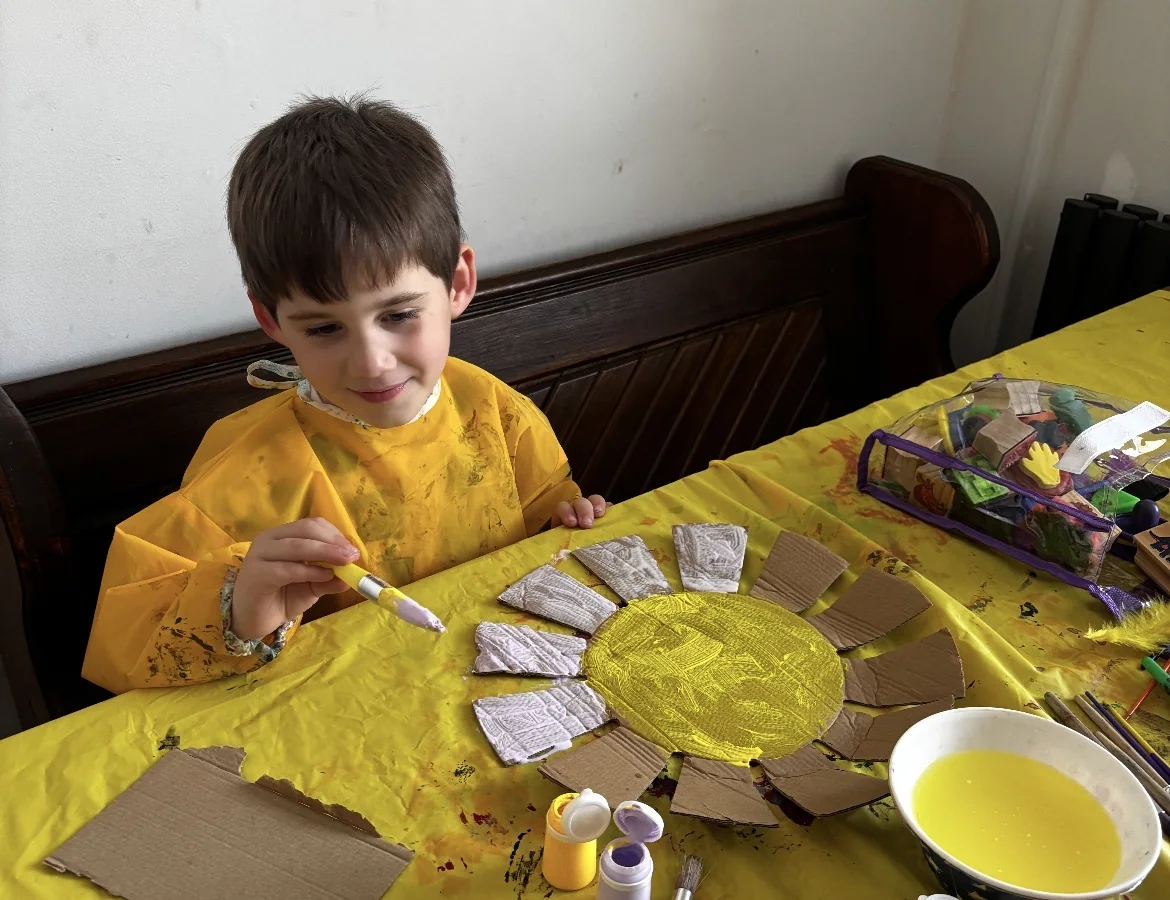 A young Creator painting a large handmade sun prop at a craft table