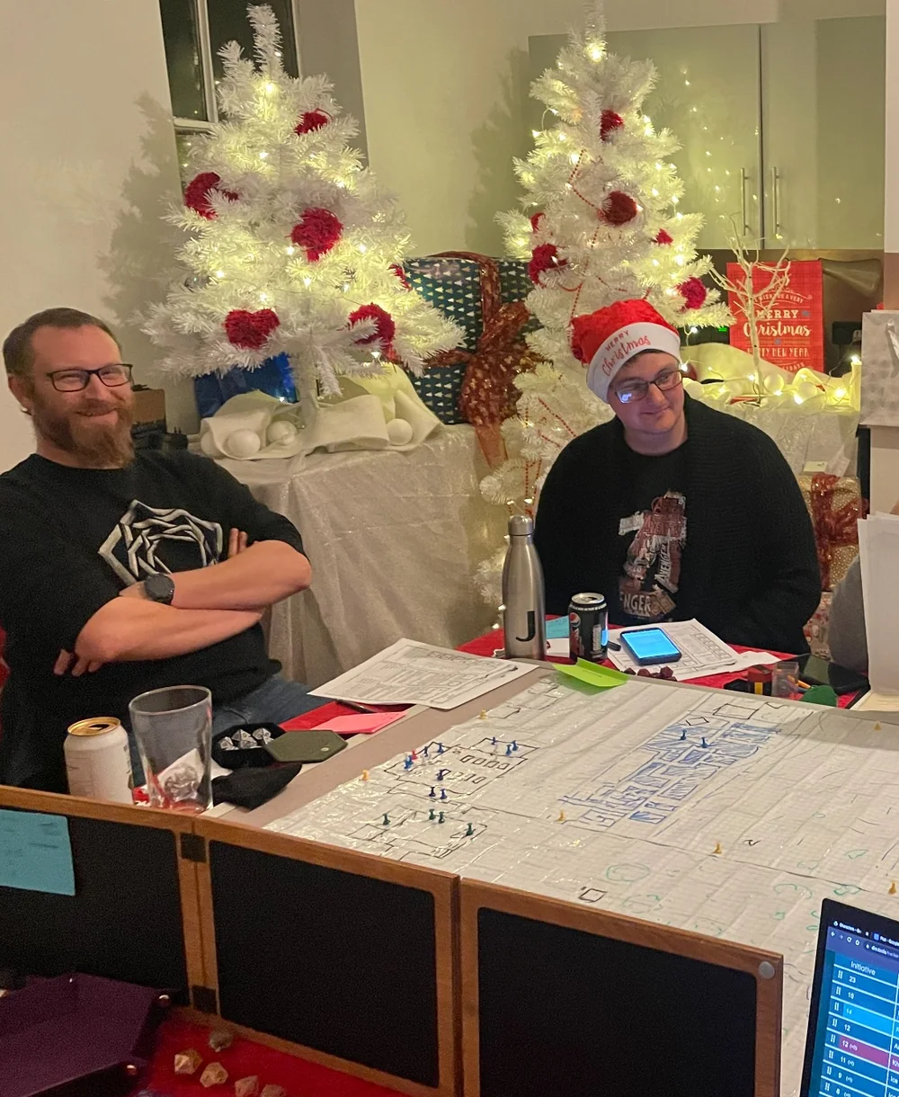 Two players sharing a festive hosted tabletop event, with the game map and Host setup visible