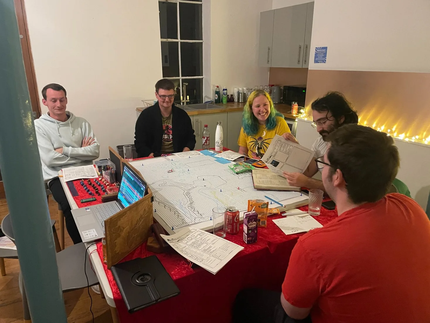Adults gathered around a tabletop roleplaying game with maps, screens and player sheets