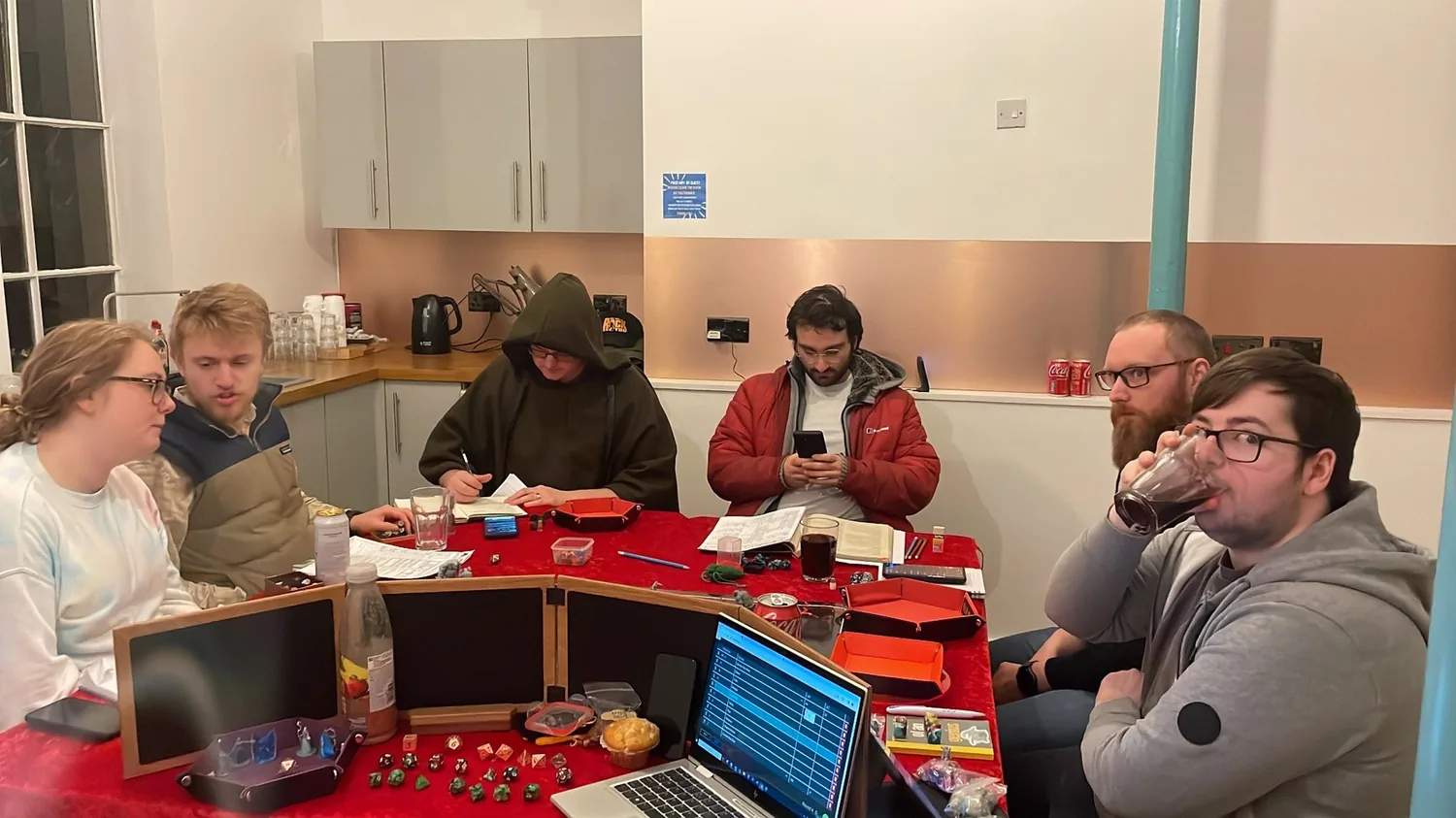 Players gathered around a tabletop roleplaying setup with dice, screens and digital Host tools