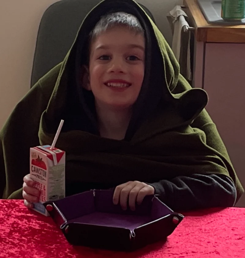 A young participant in a green fantasy cloak seated at the table, representing confidence and taking ownership of the game